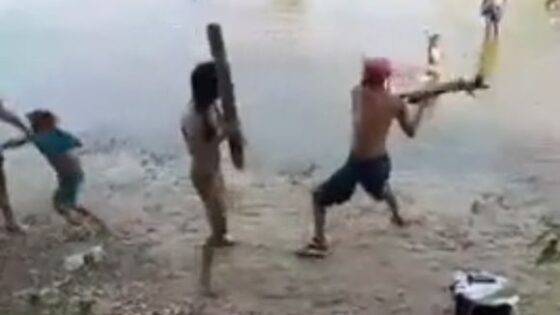 A man breaks a piece of wood off a womans head and throws her into the river Photo 0001 Video Thumb